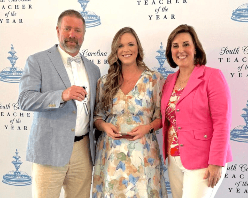 Photo of Braden Wilson with South Carolina Teacher of the Year 2025 award, standing in between with South Carolina Superintendent of Education Ellen Weaver, right, and BMW Fleet Communications Specialist Greg Bunner.