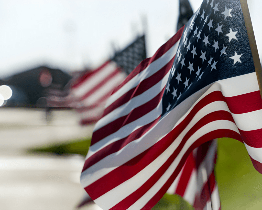 Close up shot of row of American flags posted in yard, swaying in the wind.