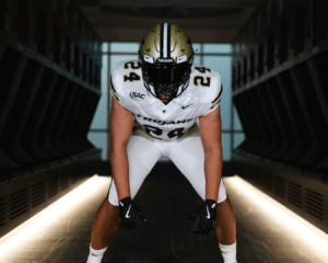 Anderson University football player wearing uniform, leaning over in front of camera in dark locker room.